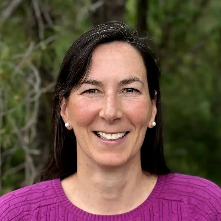 Woman smiling outdoors in a purple sweater.